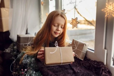 Beautiful young girl opening a gift by the window